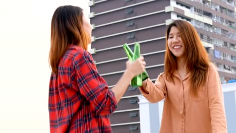 Mujer-asiática-joven-pareja-de-lesbianas-bailando-y-tintineantes-botellas-de-cerveza-fiesta-en-la-azotea.