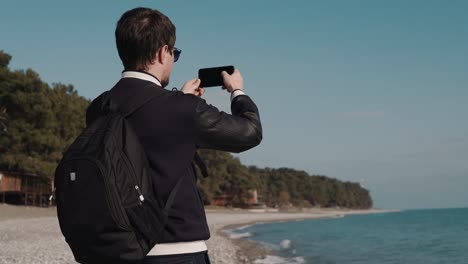 man-makes-a-series-of-photos-on-the-background-of-the-sea,-he-can-be-a-tourist