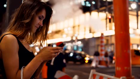 Mujer-joven-feliz-con-bolsas-de-pie-junto-a-la-pipa-de-humo-en-el-centro-de-tráfico-de-Nueva-York-y-el-uso-de-smartphone