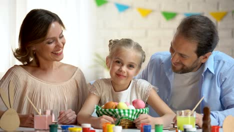 Caring-parents-kissing-little-daughter,-break-during-preparation-for-Easter-fest