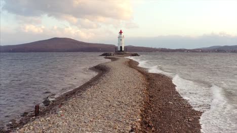 Flying-low-along-the-spit-and-ocean-waves-towards-the-lighthouse.-Aerial