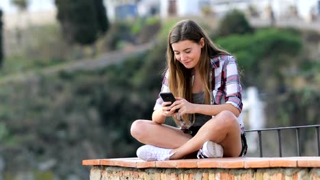 Happy-teenage-girl-browsing-phone-content-on-a-ledge