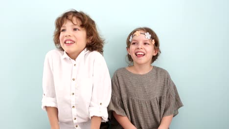 Studio-portrait-of-cute-school-children-with-wooden-signs.-Spring-holidays,-pastel-colors.-The-boy-is-wearing-a-white-shirt,-a-beige-dress-and-a-wreath-with-flowers