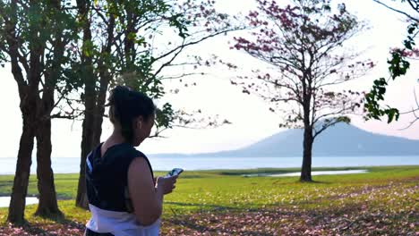 An-Asian-woman-walking-in-natural-sunlight-in-the-evening-and-listening-to-music.--concept-health-with-exercise.-Slow-Motion