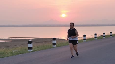 Übergewichtige-asiatische-Frauen-joggen-am-frühen-Morgen-im-Sonnenlicht-auf-der-Straße.-Konzept-des-Gewichtsverlustes-mit-Bewegung-für-die-Gesundheit.-die-Zeitlupe