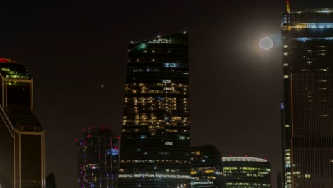 The-moon-rising-over-the-illuminated-highway-and-the-night-city,-time-lapse