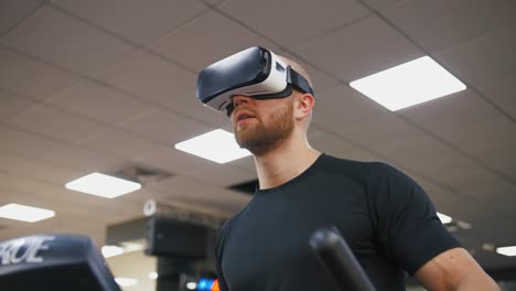 Young-strong-man-exercising-on-treadmill-at-the-gym,-wearing-VR-glasses