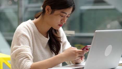 Hübsche-asiatische-Frau-mit-Handy-und-Laptop-im-Innenbereich