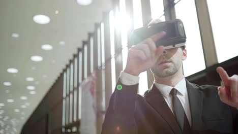 Modern-middle-aged-businessman-in-formal-suit-and-tie-wearing-VR-headset,-exploring-and-swiping-data-visualized-in-virtual-reality-in-sunlight