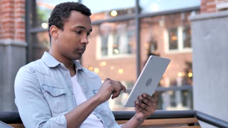 Hombre-africano-sentado-al-aire-libre-y-usando-la-tableta