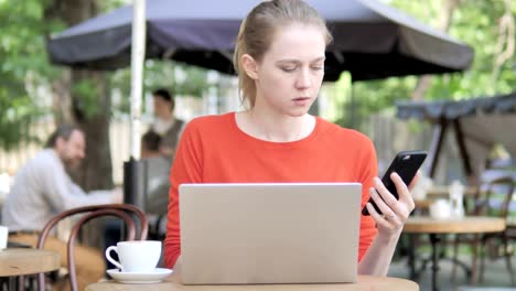 Junge-Frau-nutzt-Smartphone-und-Laptop-Sitting-in-Café-Terrasse