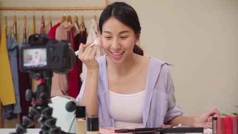 Slow-motion---Beauty-blogger-present-beauty-cosmetics-sitting-in-front-camera-for-recording-video.-Happy-beautiful-young-Asian-woman-use-cosmetics-review-make-up-tutorial-broadcast-live-video.