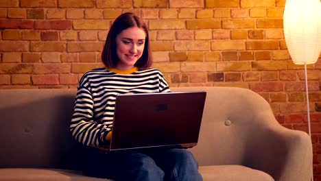 Closeup-portrait-of-young-pretty-girl-using-the-laptop-sitting-on-the-couch-in-a-cozy-apartment-indoors