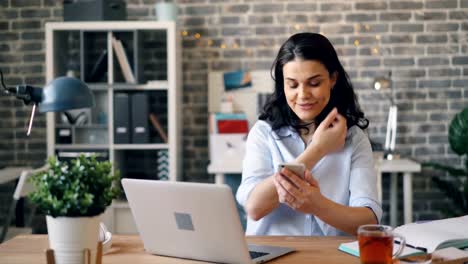 Smiling-girl-using-smartphone-watching-content-on-screen-in-workplace