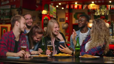 Un-gran-grupo-de-amigos-en-el-bar-sentadoen-en-la-mesa-riendo-y-charlando-bebiendo-cerveza