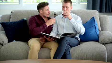 Gay-couple-relaxing-on-couch.-Wide-shot.-Toast-together.