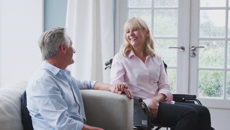 Senior-Paar-mit-Frau-im-Rollstuhl-sitzen-in-der-Lounge-zu-Hause-reden-und-lachen-zusammen