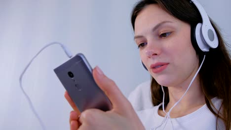 La-mujer-está-escuchando-música-en-auriculares-en-el-teléfono-inteligente-y-cantando-una-canción.