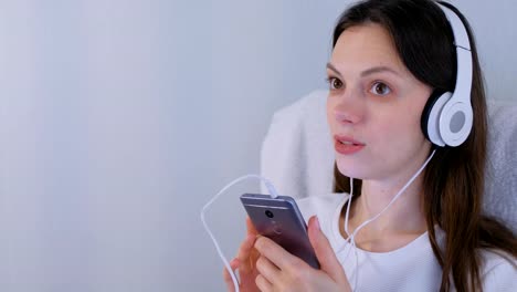 La-mujer-está-escuchando-música-en-auriculares-en-el-teléfono-inteligente-y-cantando-una-canción.