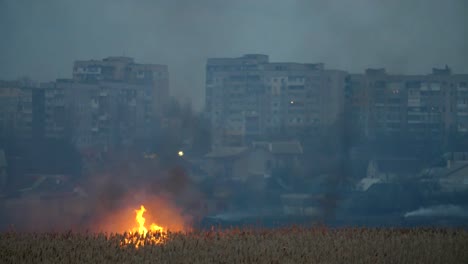 Überraschende-Aussicht-auf-mehrstöckige-Wohnblocks-am-Dnipro-Flussufer-und-das-stürmische-Feuer-über-den-Fluss-im-Sedge-Feuchtgebiet-im-Frühjahr