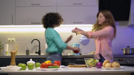 Positive-sisters-moving-to-music-dancing-together-in-kitchen,-having-fun-at-home