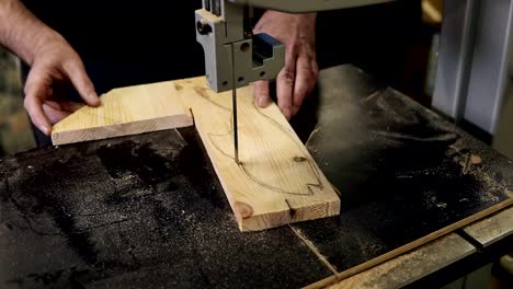 Close-up-footage-of-male's-hands-working-with-an-electric-cutting-machine.-High-angle-footage-of-a-man-cutting-a-fish-shape-wooden-pattern-on-a-table