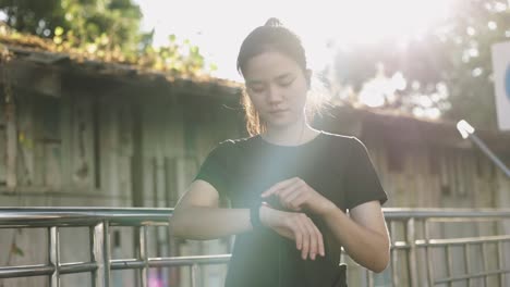 Attraktive-junge-asiatische-Sportlerin,-die-mit-Herzfrequenz-auf-einer-Smartwatch-checkt.-Jogging-Workout-Lifestyle-auf-der-Straße-bei-Sonnenuntergang.