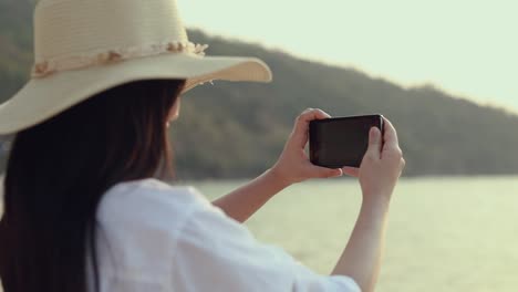 Feliz-mujer-adolescente-asiática-sosteniendo-el-teléfono-inteligente-tomando-una-foto-en-la-playa-hermosa-puesta-de-sol.-Concepto-de-vacaciones-de-vacaciones-de-viaje-estilo-de-vida.