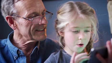 Primer-plano-de-nieta-con-el-abuelo-en-la-silla-jugando-en-la-tableta-digital-en-casa-juntos