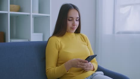 Mujer-usando-el-teléfono-inteligente.-Chica-bonita-usando-la-pantalla-de-toque-del-teléfono-inteligente-moderno-y-sonriendo-en-casa