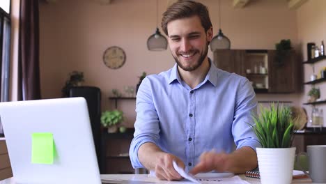 Smiling-happy-businessman-using-laptop,-holding-smartphone,-talking-on-cell-phone-sits-at-desk,-making-business-call-at-home-office.