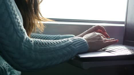 Weibliche-Hände-Tippen-auf-Tastatur-von-Laptop-im-Zug.-Frau-während-der-Eisenbahn-unterwegs-mit-Freunden-chatten.-Junges-Mädchen-mit-Notebook.-Arm-drucken-Sie-eine-Nachricht.-Nahaufnahme