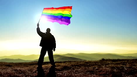 Exitosa-silueta-hombre-ganador-ondeando-Gay-homo-bandera-sobre-la-cima-de-la-montaña,-4-k-cinemagraph