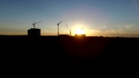 Aerial-shot-of-crans,-building-and-forest-at-sunset.