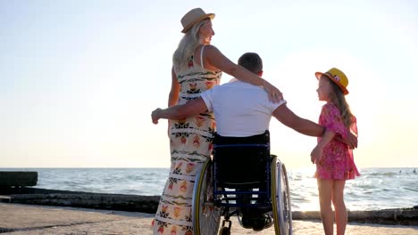 invalid-with-pregnant-woman-and-child-on-background-sea,-husband-in-wheelchair-hug-wife-with-big-belly