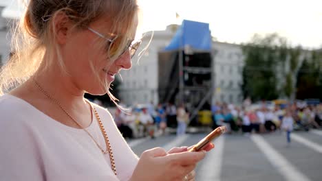 süße-Frauen-in-Gläser-hält-Smartphone-in-Händen-und-lächelte-im-freien-Innenstadt-in-Sonnenstrahlen