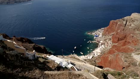 White-houses-lying-on-top-of-mountain-on-Santorini,-bay-at-bottom-of-red-cliff