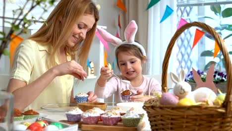 Joven-madre-y-su-hija-con-orejas-de-conejo-cocinar-cupcakes-de-Pascua