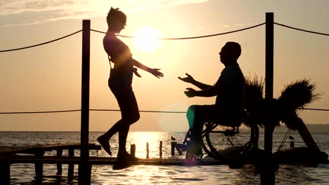 Silhouette-des-behinderten-Mann-und-Frau-gegen-Sonne,-romantische-Treffen-am-Wasser