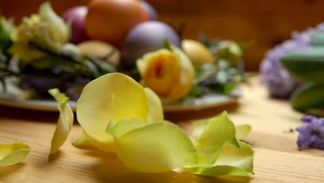 Petals-of-rose-fall-on-a-table-against-a-background-of-colored-Easter-eggs