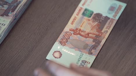 Female-hand-touches-five-thousand-ruble-banknote-on-table