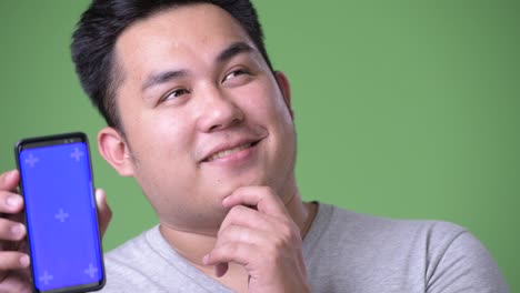 Young-handsome-overweight-Asian-man-against-green-background