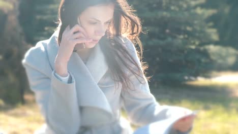 Portrait-of-buisness-woman-sitting-in-the-spring-park-on-the-grass-and-talking-on-a-mobile-phone.