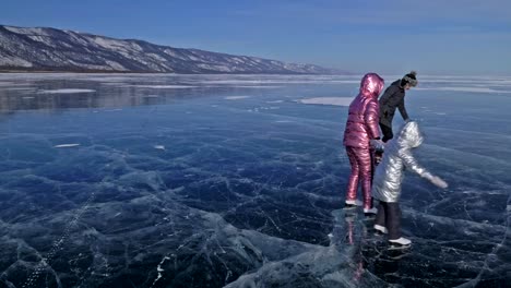 Family-is-ice-skating-at-day.-Girls-to-ride-figure-ice-skates-in-nature.-Mother,-daughter-and-son-riding-together-on-ice-in-cracks.-Outdoor-winter-fun-for-athlete-nice-winter-weather.