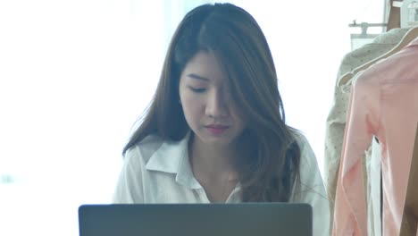 Beautiful-young-smiling-woman-working-on-laptop-while-enjoying-drinking-warm-coffee-sitting-in-a-living-room-at-home.-Enjoying-time-at-home.-Asian-business-woman-working-in-her-home-office.