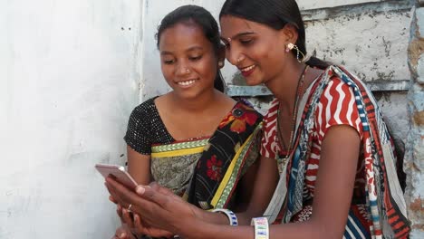 Two-Indian-girls-in-a-village-house-in-rural-Indian-share-laugh-on-mobile-phone-forward-video-joke-emoji-photo-on-their-touch-screen-funny-hilarious-busy-occupied-laughter-company-teamwork-bonding