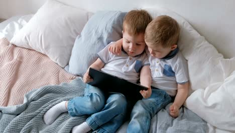 Kids-with-tablet.-Two-boys-twins-toddlers-looking-cartoon-at-tablet-lying-on-the-bed.