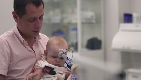 Papa-hält-ein-Baby-mit-medizinischen-Sensoren-an-Händen