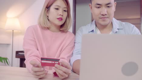 Young-Asian-family-couple-using-laptop-discussing-news-or-doing-online-shopping-sitting-together-on-desk-at-home-on-weekend-together,-serious-man-and-woman-browsing-web-searching-for-new-sale-offers.