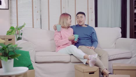 Attraktive-asiatische-süße-paar-Momente-Liebe-trinken-heißen-Tasse-Kaffee-oder-Tee-in-der-Hand-auf-Sofa-im-Wohnzimmer-zu-Hause.-Ehemann-und-Ehefrau-zu-Hause-entspannen-Konzept.